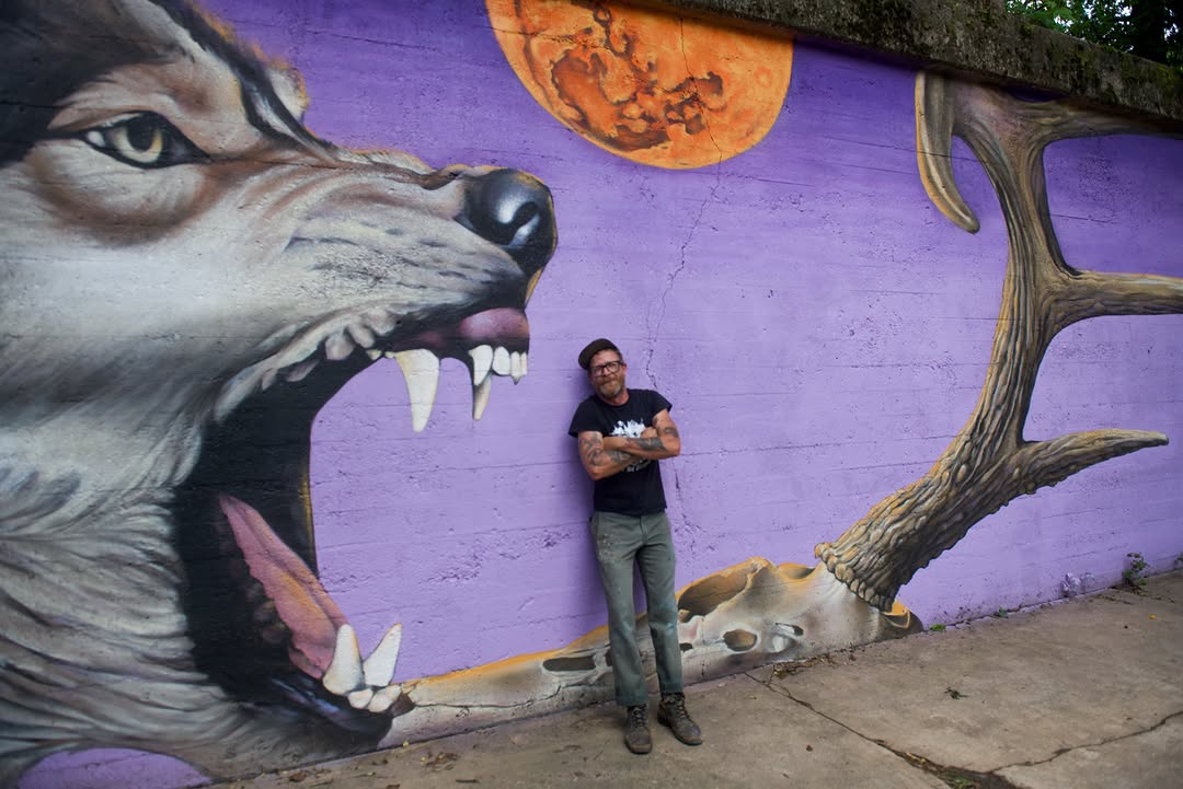 Samuel Hale standing beside the Survival wolf mural under the 6th Street Bridge in Little Rock